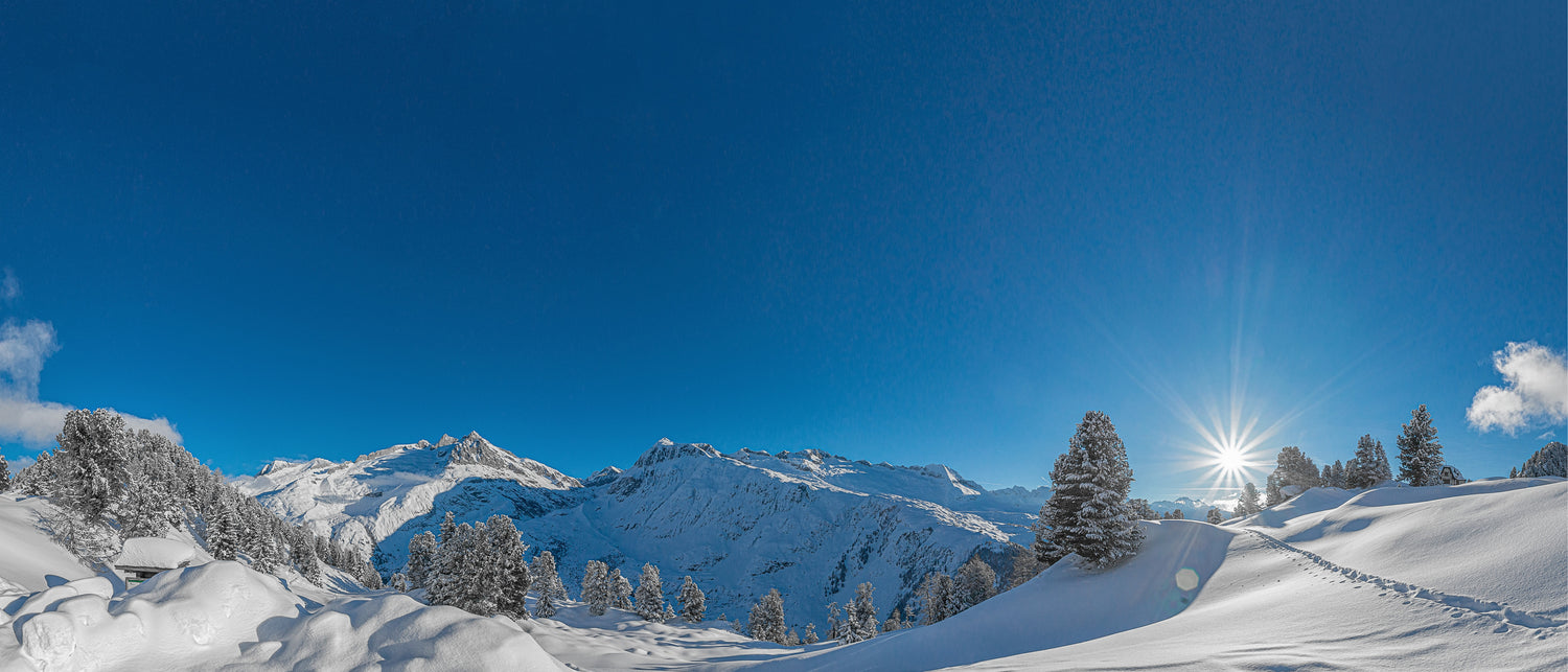Paysage d'hiver ensoleillé. Vue de somments de montagnes avec quelques sapins enneigés et un soleil radieux à droite. On voit un ciel bleu immaculé. Une parfaite journée d'hiver!